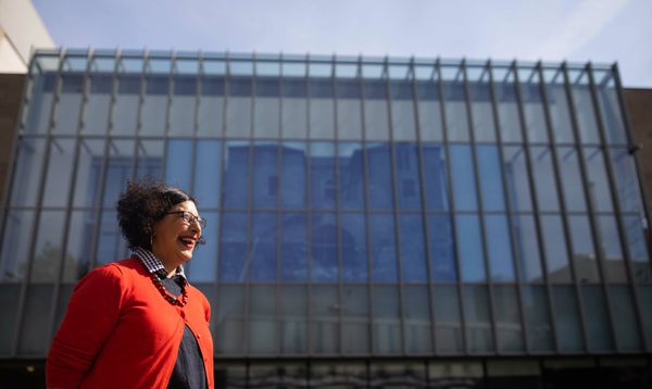 A woman in an orange cardigan stands in front of The Studio at Festival Theatre with an art installation in the window behind her