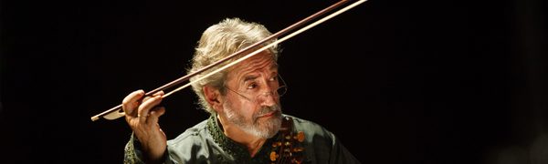 The conductor pictured seated behind a music stand, holding his viol in one hand and gesturing with the bow in his other.