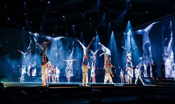 A group of acrobats stand holding other acrobats in handstands above their head