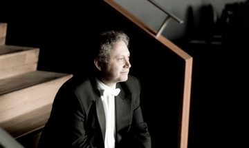 A man in a suit sits on a wooden staircase, gazing out into the distance.