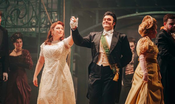A prince and a woman in a ball gown dance holding hands