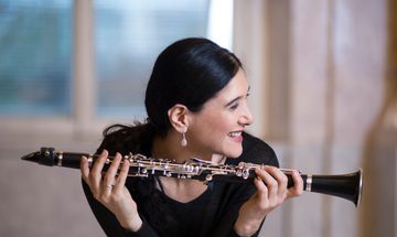 A smiling woman holds a clarinet lengthways in both hands, looking off to the side.