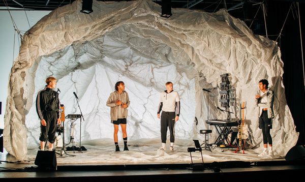A group of young men stand on stage under a dome of crinkled material