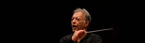 The conductor shown mid-performance, holding his baton on a darkly lit stage