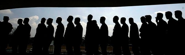 A group of men stand in a line in silhouette, with a strip of blue sky visible behind them