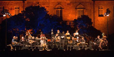 The early music ensemble performs outside against a dramatically lit historic building