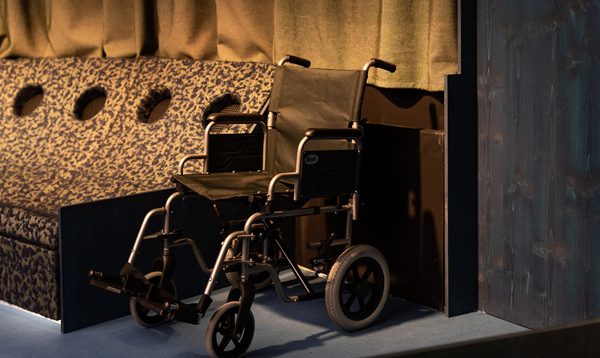 A wheelchair pictured next to a row of reclined black seating in a circular space lit from above.