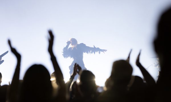 A woman is lit in shilouette as she sings into a microphone and poses with her arm oustretched