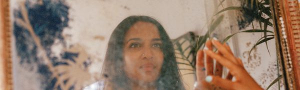 Dressed in a white dress with straight hair, the singer touches her reflection in a smudged, ornate mirror.