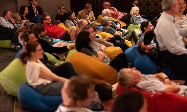 Audience members sit in colourful beanbags amongst orchestra members, smiling and listening