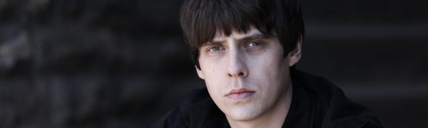 A man in a black jumper, looks at the camera with a serious face