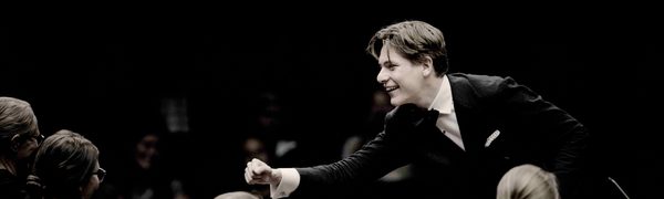 Conductor Klaus Makela leans forward and smiles as he conducts the Oslo Philharmonic