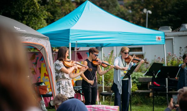 Musicians play under a blue marquee outside of a hospital. Patients and hospital staff watch.
