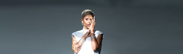 A woman with short hair partially covers her face with her hands. She wears a crisp white shirt.