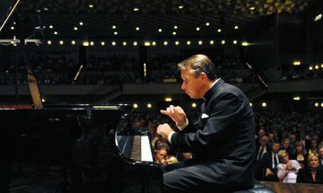 Mikhail Pletnev plays piano with a full concert hall in the background