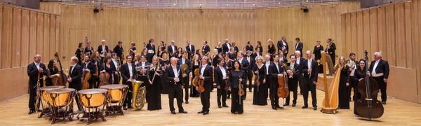All of the members of the RSNO stand on a stage wearing formal dress with their instruments