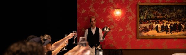 A waiter stands holding a tray behind a table full of people raising their glasses