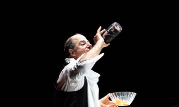 A man in a suit drinks wine straight from the bottle while holding a glass bowl