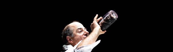 A man in a suit drinks wine straight from the bottle while holding a glass bowl