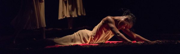A dancer lies on a red silk dress, she holds her upper body up above the ground with her arms.