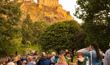 A group of people enjoying music in Princes Street Gardens with the castle in the background