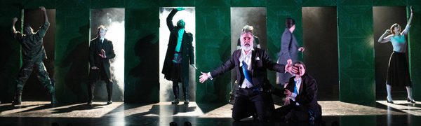 A man keels on a misty stage with a series of doors in the background with his arms outstretched