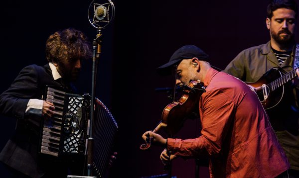 Three men perform on stage, with fiddle, accordion and tenor guitar