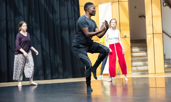 A man dances in a studio as two women watch