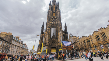 The front of The Hub, a neo-gothic church at the top of the Royal Mile, with many people walking in front of it