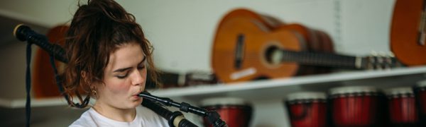 A woman in a white t-shirt with brown reddish hair piled on top of her head plays the Scottish smallpipes