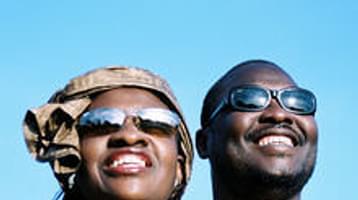 Man and woman wearing sunglasses staring into the sun with blue background