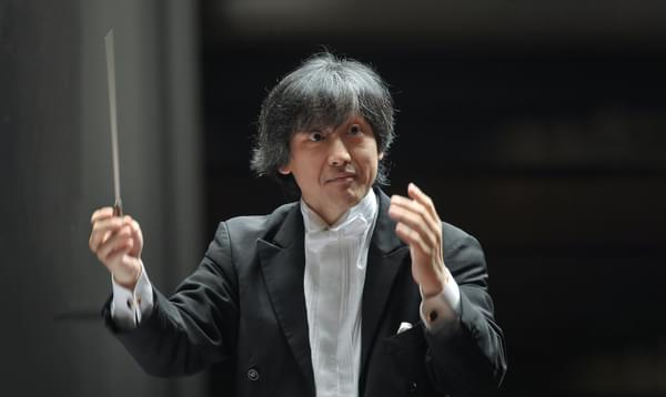 Conductor Kazushi Ono pictured holding his baton, wearing a black tuxedo