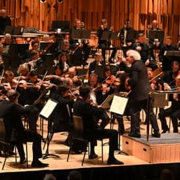 An orchestra dressed in black tie performing onstage, conducted by Sir Simon Rattle