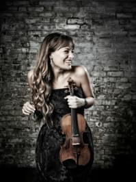 Nicola Benedetti looking to the left and smiling while holding her violin.