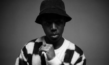 Moses Boyd poses in a black hat and black-and-white checked sweater