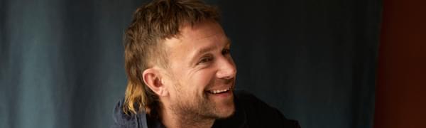 Damon Albarn pictured seated with blue jacket and mullet hairstyle