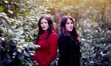 Rachel and Becky Unthank stand back to back in a forest