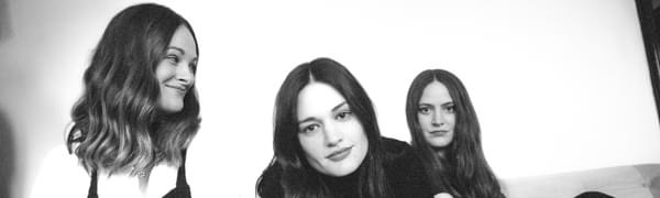 Black and white photo of the three sisters of The Staves, posing on a sofa