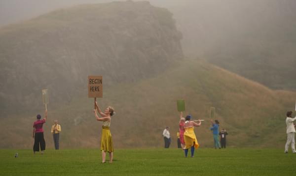 Colourfully dressed figures shrouded in mist hold up placards against the backdrop of Arthur's Seat
