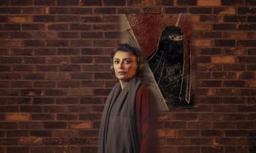A woman wearing headphones stands facing the camera, in front of brick wall featuring a painting of a woman wearing a niqab.