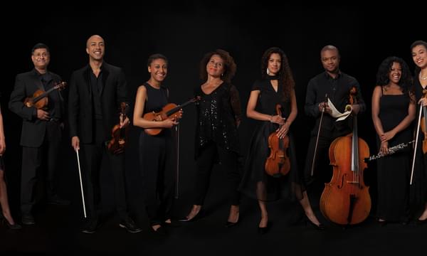 Members of the Chineke! Orchestra stand with their instruments, with Chi-chi Nwanoku standing in the middle