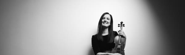 Black and white image of Jenna Reid sitting with her violin