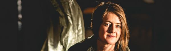 Karine Polwart sits cross-legged on the floor, with green fabric draped over her.