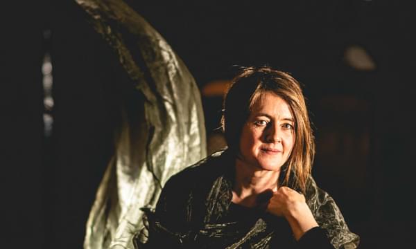 Karine Polwart sits cross-legged on the floor, with green fabric draped over her.