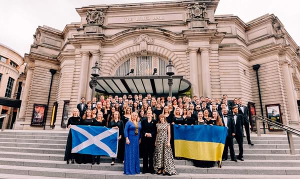 An orchestra stands in front of Usher Hall holding a Scottish flag and a Ukrainian flag