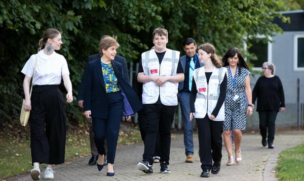 Nicola Sturgeon walks along a path talking to a group of Leith Academy students in Muster Station Front of House uniforms