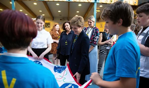 Nicola Sturgeon looks and smiles at a quilt held by a group of Leith Academy students