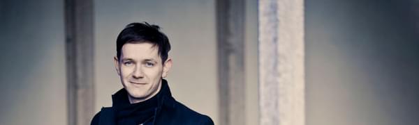 The singer pictured wearing a navy coat and matching scarf, looking directly into the camera.