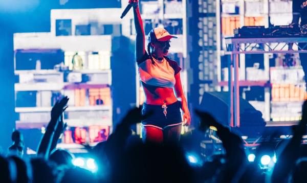 A woman stands on stage in front of applauding fans, holding a mic above her head and projections of blocks of flats behind her.