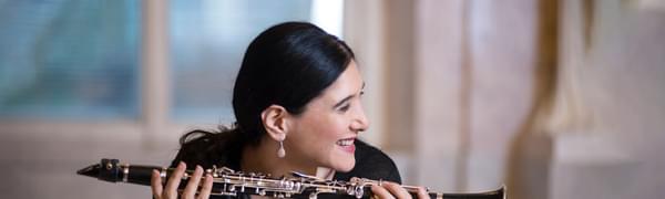 A smiling woman holds a clarinet lengthways in both hands, looking off to the side.